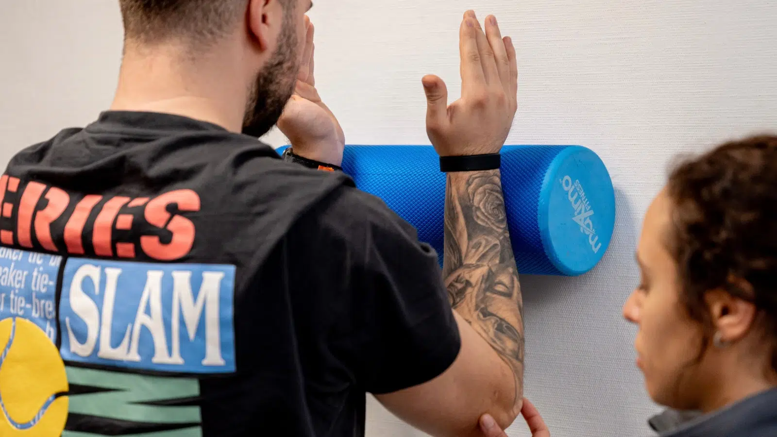 Patient nutzt eine Faszienrolle an der Schulter unter physiotherapeutischer Anleitung.